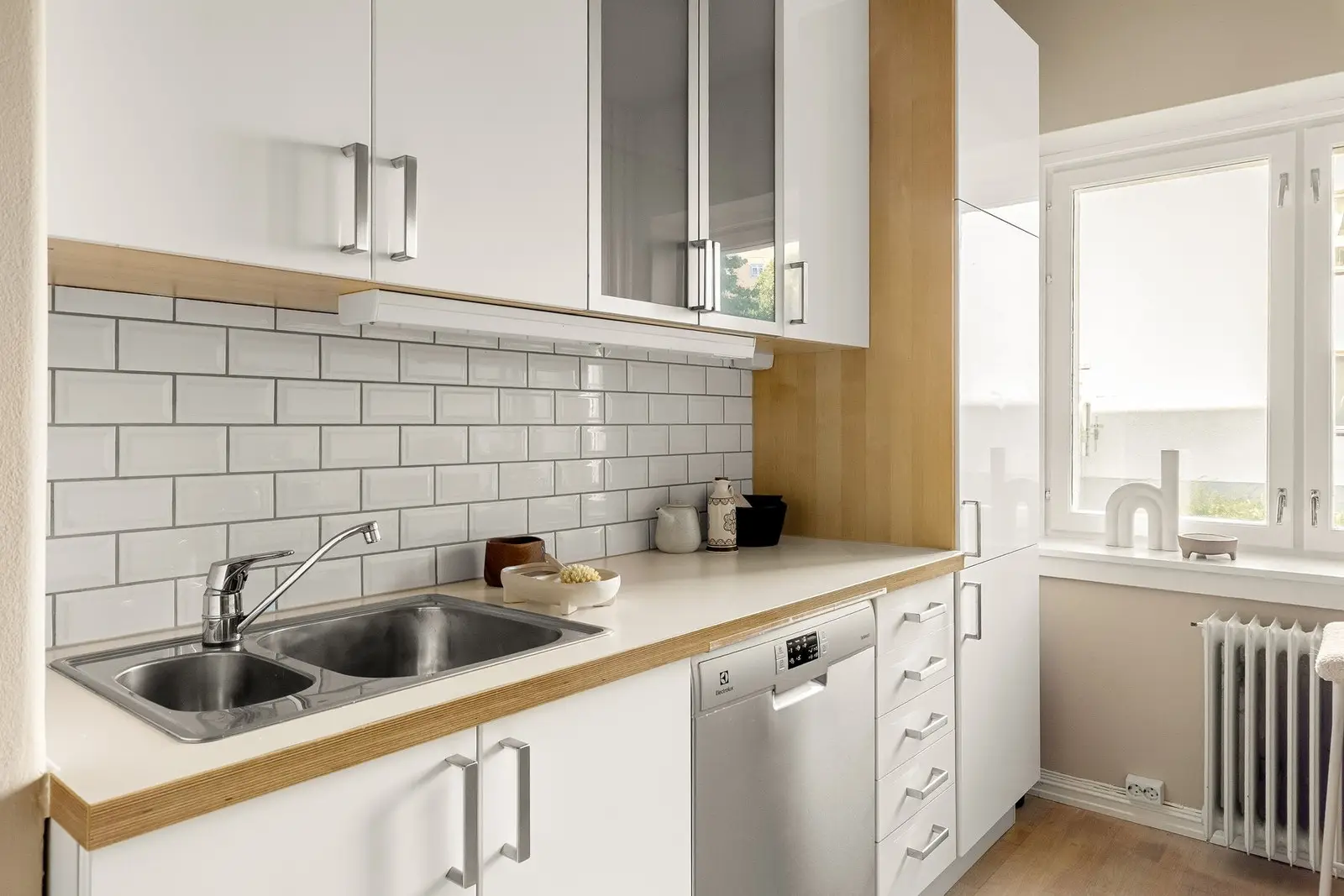 Kjøkkeninnredningen er utstyrt med hvite glatte fronter, vitrinedører med frostet glass, benkeplate i laminat med nedfelt kum i rustfritt st